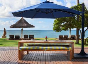 a wooden bench with a blue umbrella and a table at Tivoli Ecoresort Praia do Forte in Praia do Forte