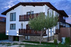 a white house with wooden balconies and a tree at Къща Александра 2 in Dobrinishte