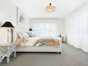 a white bedroom with a bed and a chandelier at Shelley Beach Retreat Kilcunda in Kilcunda