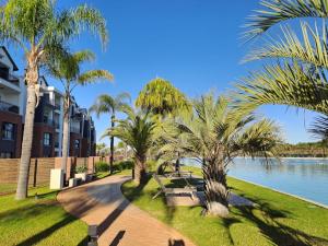 a walkway with palm trees and benches next to the water at Luxury beach lagoon 1 Bedroom apartment in Pretoria