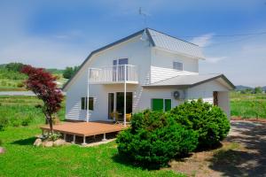 a white house with a deck in the yard at HOKKAIDO VILLA e2 in Nakafurano
