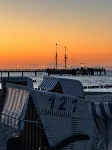 a beach with chairs and a pier at sunset at Morada Strandhotel Ostseebad Kühlungsborn in Kühlungsborn
