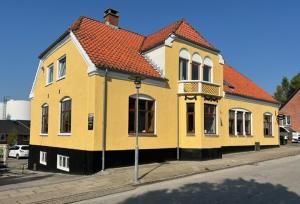 un bâtiment jaune avec un toit orange dans une rue dans l'établissement Folsted - Værelse 201 fri parkering, à Bindslev