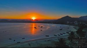 a sunset on a beach with boats in the water at 11Suites casa Suite #8 in Caraguatatuba