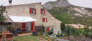 a house with red windows and a white umbrella at La Fischaumière in Soleilhas