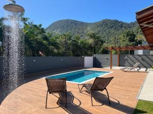 einen Pool mit zwei Stühlen und einem Brunnen in der Unterkunft Casa Mero no Residencial Mar Verde em Caraguatatuba in Caraguatatuba