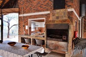 a brick kitchen with a table and a fireplace at Elijara Kruger Lodge in Marloth Park