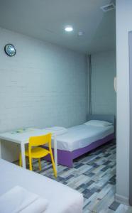 a room with two beds and a table and a yellow chair at City Hostel Shymkent in Shymkent