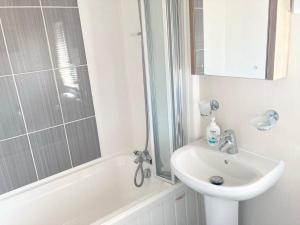 a white bathroom with a sink and a bath tub at Vogue at Primrose in Reighton