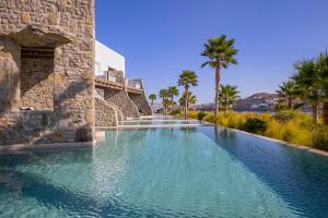 a swimming pool with blue water and palm trees at Aeonic Suites and Spa in Mýkonos City