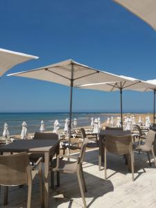 a group of tables and chairs with umbrellas on a beach at Villa della Concordia in Plaia Grande