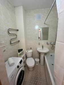 a bathroom with a toilet and a sink and a washing machine at Уютная квартира в центре города in Taldykolʼ