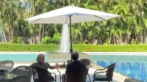un hombre y una mujer sentados en una mesa bajo un paraguas junto a una piscina en The Palms At Coco Beach, en Coco