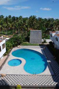 a large swimming pool in a yard with palm trees at Malpe Sea Front Cottages in Udupi