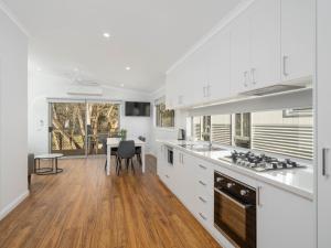 a kitchen with white cabinets and a dining room with a table at Painters Island Holiday Park in Wangaratta