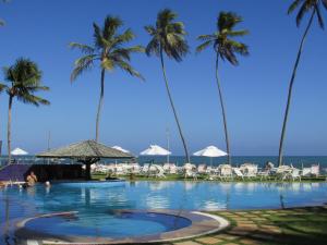 a swimming pool with palm trees and the ocean at Praia do Forte Condomínio Bali Bahia Apt105 in Praia do Forte