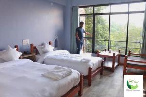 un uomo in piedi in una stanza d'albergo con due letti di Hotel Dhulikhel View Point a Dhulikhel