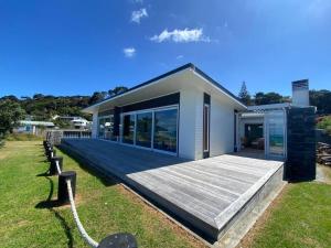 a house with a wooden deck in the yard at Rangi Beachfront -Luxury Beachfront Bach in Karikari Peninsula