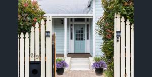 a white house with a blue door and flowers at Blue Wren Cottage on Edith - A Fireside Retreat in Wine Country in Cessnock