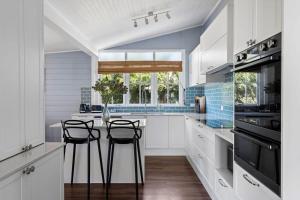 a kitchen with white cabinets and a table with stools at Blue Wren Cottage on Edith - A Fireside Retreat in Wine Country in Cessnock