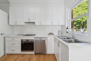 a kitchen with white cabinets and a sink and a window at Blu Ocean Views Collaroy - Sunroom & BBQ in Collaroy