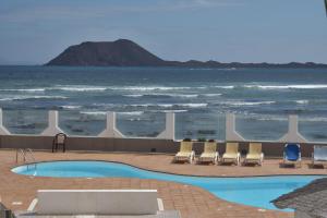 a swimming pool with chairs and the ocean in the background at Almina in Corralejo
