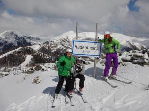 drei Menschen auf Skiern stehen neben einem Schild auf einem Berg in der Unterkunft Bio Naturhof Ottingerhof in Bad Kleinkirchheim