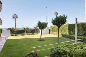 Un jardín con palmeras y el océano al fondo. en SeaHomes Vacations - Seafront Apt Fenals with PKG, en Lloret de Mar