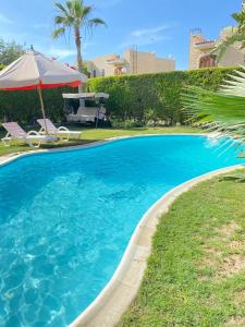a large blue swimming pool with an umbrella and chairs at فيلا بحمام سباحة مارينا 6 الساحل الشمالي العلمين in El Alamein