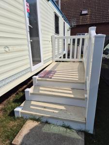 a porch with a white railing and stairs next to a house at Sandgate retreat hemsby 2023 in Hemsby