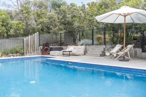 a swimming pool with an umbrella and chairs and a couch and an umbrella at The Dreaming in Saint Andrews Beach