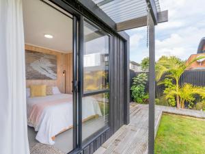 1 dormitorio con puertas de cristal y 1 cama en el balcón en Sunny Hideaway - Whangamata Holiday Home, en Whangamata