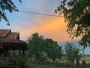 a sunset over a house with trees in the foreground at Chanmolfarmstay in Phumĭ Chŭb Chănt Sâr +10 photos