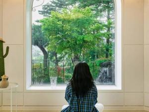a woman sitting on a chair looking out of a window at Gangneung Gangneung Love Pension in Gangneung