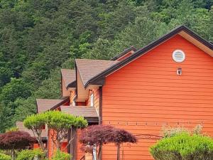 a red house with trees in front of a mountain at Eoullim Pension - Moonlight Yard in Pyeongchang