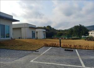 a building with a parking lot next to a field at Jeju Bijarim Very Mung Pension in Jeju