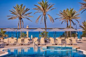 Un resort con piscina, sillas y palmeras. en Universal Hotel Neptuno - Adults Only, en Playa de Palma