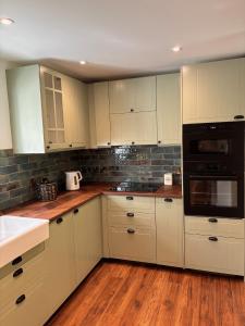 a kitchen with white cabinets and black appliances at The Cottage, Walworth Demesne in Ballykelly