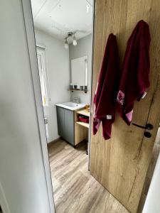 a bathroom with a sink and red towels on a door at Mobile-home 3 chambres chaleureux et calme in Seillac +9 photos