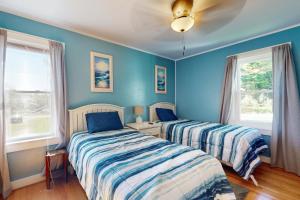two beds in a room with blue walls and windows at Goose Creek Cottage in North Lamoine