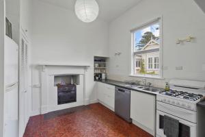 Biała kuchnia z kuchenką i oknem w obiekcie Hewlett Cottage w mieście Port Fairy +9 zdjęć