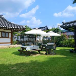 a picnic table with two white umbrellas and a grill at Yeongam Haeden Hanok Stay in Yeongam