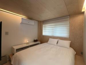 a bedroom with a white bed and a window at Gangchon 1225 Pension in Chuncheon