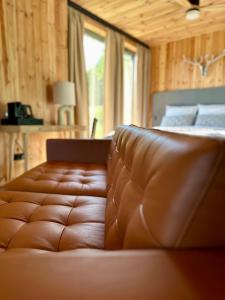 a brown leather couch in a bedroom with a bed at Brown Deer - z Sauną na Tarasie, Jacuzzi i Widokiem na Góry - by Deer Hills Luxury Apartments in Kocoń