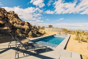 a swimming pool with two chairs and a rock wall at Bolder House By The Cohost Company in Joshua Tree