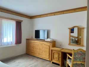 a living room with a tv on a wooden dresser with a mirror at Sporthotel Oberwald in Oberwald