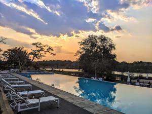 a pool with chairs and a sunset in the background at Baluba Game Resort in Luanshya