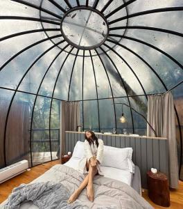 a woman sitting on a bed in a room with a clock at Cabana Bolha Urubici in Urubici