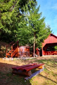 a wooden bench in front of a red barn at Cabană în inima munților - Gálkuti Kulcsosház in Bălan