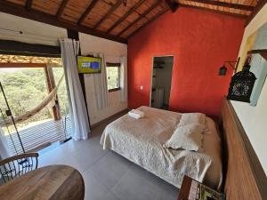 a bedroom with red walls and a bed and a table at Chalés Vila Real - Tranquilidade na Serra de Carrancas - Piscina com uma vista espetacular do Pôr do Sol in Carrancas